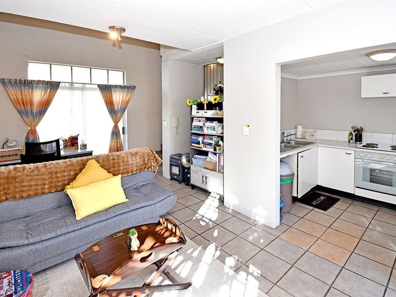 Open-plan living area featuring tiled floors, an exposed brick wall, and a functional kitchen with built-in cabinetry, oven, and hob.