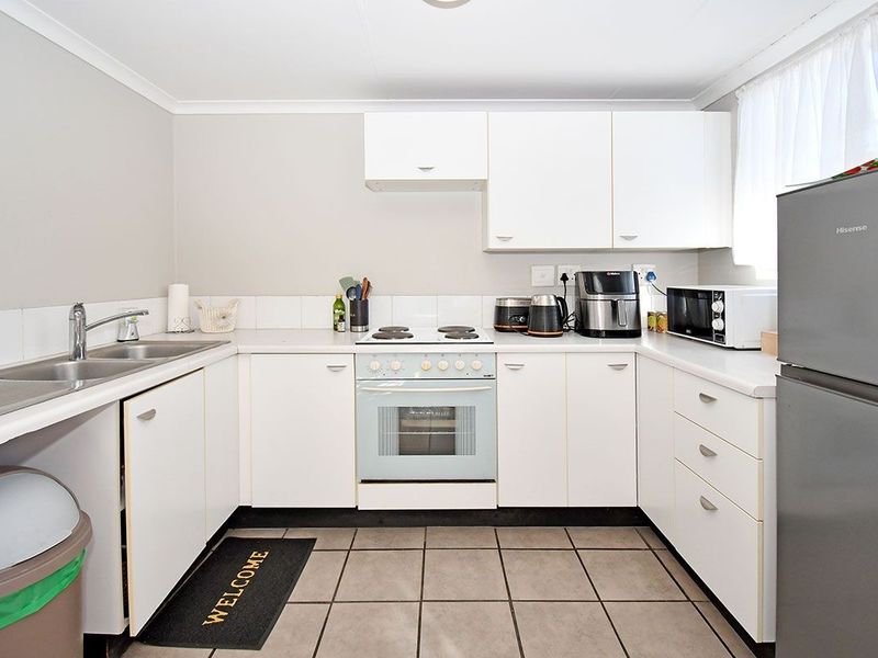 A functional kitchen featuring white cabinetry, tiled flooring, a built-in oven and stove, and a double sink with a tiled backsplash.