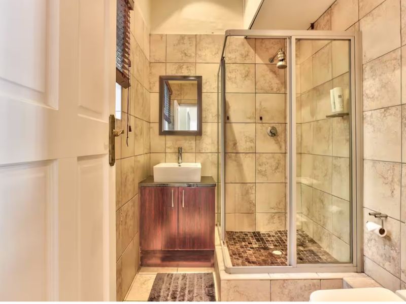 A compact, well-maintained bathroom featuring a glass-enclosed shower, a modern vessel sink with a vanity cabinet, and neutral wall tiling.