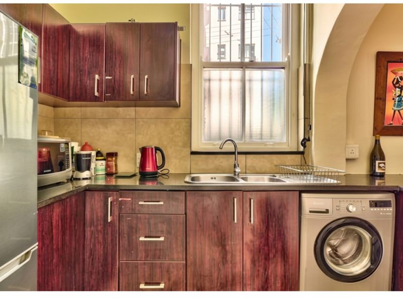 A compact kitchen featuring dark wood-look cabinetry, granite countertops, a double stainless steel sink, and an integrated washing machine.
