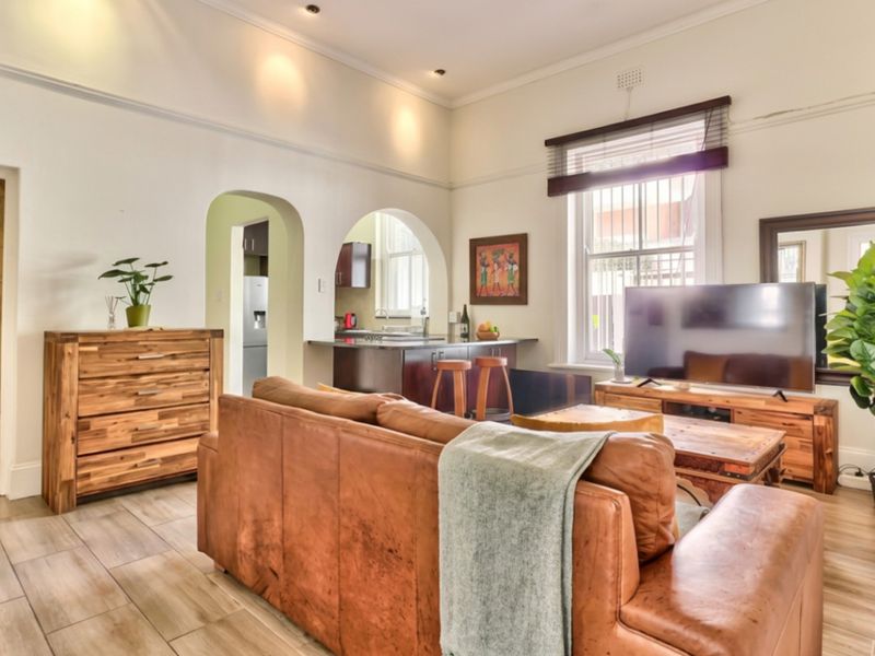 Open-plan living area featuring high ceilings, recessed lighting, and timber-look floor tiles, with an arched transition to the adjacent kitchen space.
