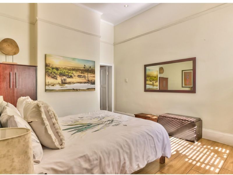A well-maintained bedroom featuring timber-look floor tiles, high ceilings with picture rails, and recessed lighting.