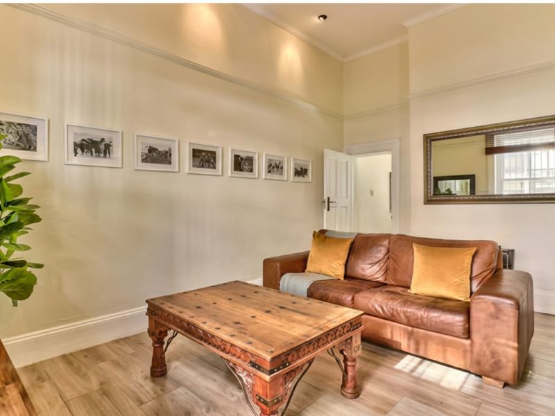 A well-maintained living room featuring laminate flooring, recessed downlighting, and classic architectural detailing including skirting boards and architraves.