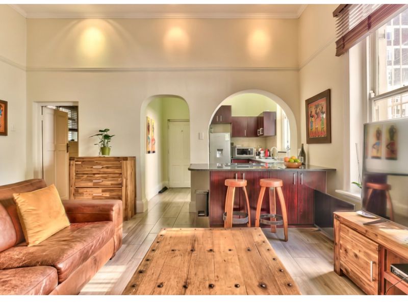 Open plan living area featuring a kitchen with dark wood cabinetry, a breakfast bar, and an arched entryway leading to a hallway.