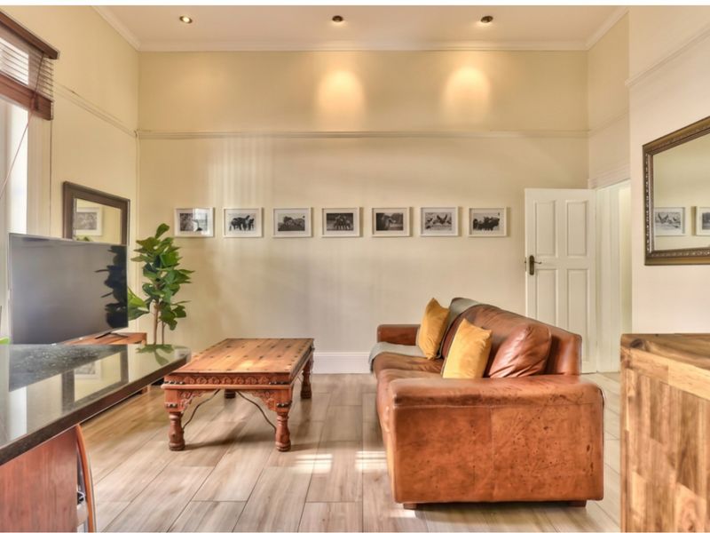 A well-maintained living room featuring high ceilings, recessed downlighting, timber-look tile flooring, and classic architectural details like picture rails.