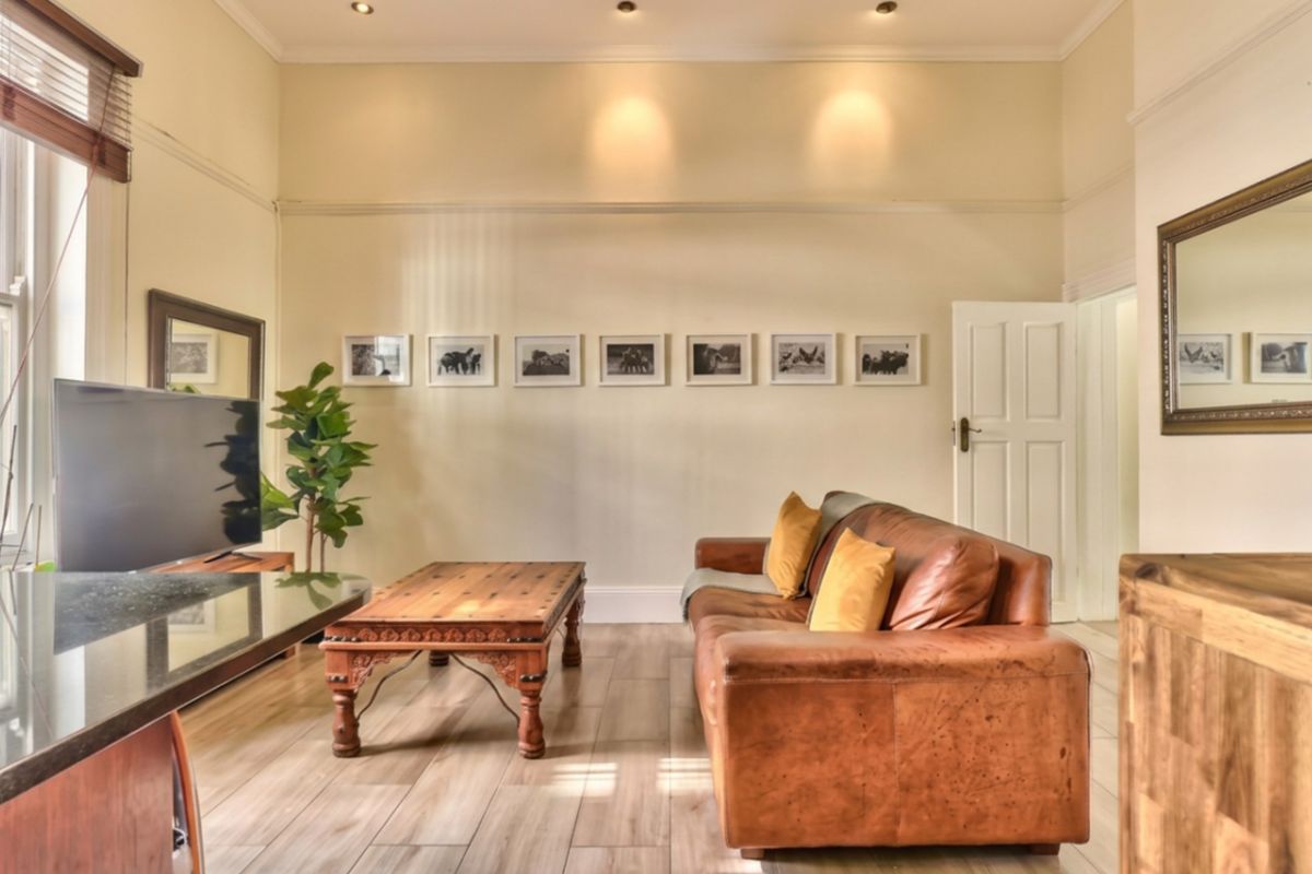 A well-maintained living room featuring high ceilings, recessed downlighting, timber-look tile flooring, and classic architectural details like picture rails.