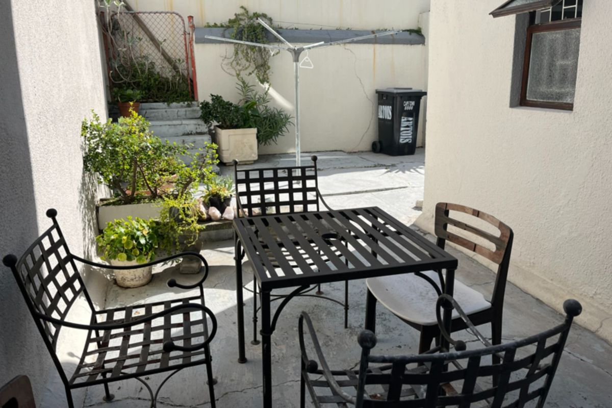 A paved rear courtyard area featuring a retaining wall, security gate, and external window access, providing a functional outdoor space.