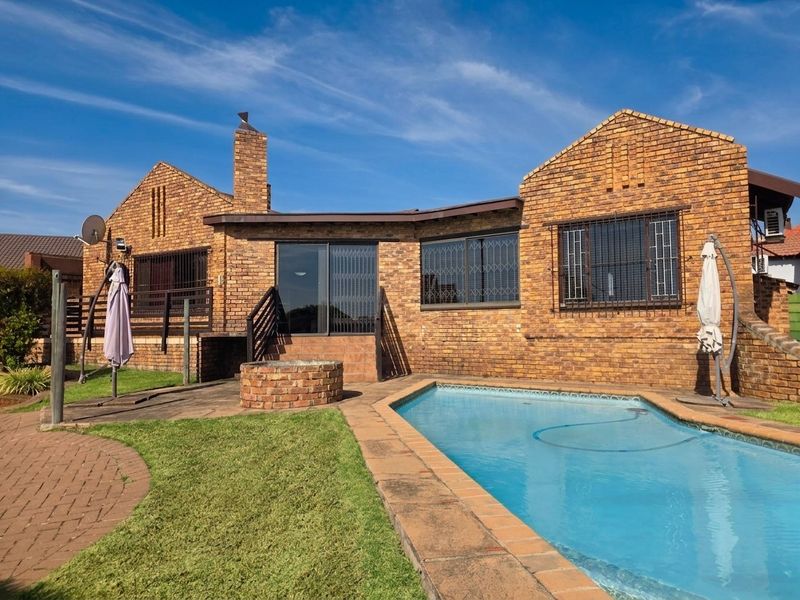 Rear exterior view of a brick house featuring a swimming pool, paved patio area, and a built-in brick fire pit.