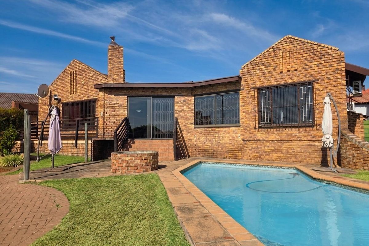Rear exterior view of a brick house featuring a swimming pool, paved patio area, and a built-in brick fire pit.