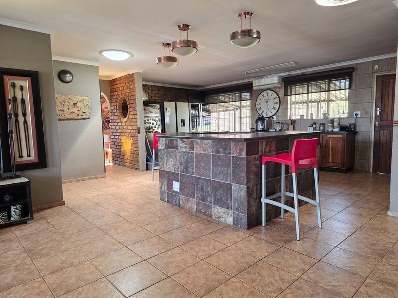 Spacious open-plan kitchen area featuring a large tiled island, ceramic flooring, exposed brick accents, and modern pendant lighting.