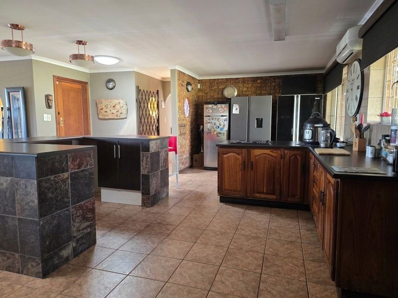 Spacious kitchen featuring wooden cabinetry, an exposed brick feature wall, tiled flooring, and a stone-tiled breakfast counter, offering a functional layout.