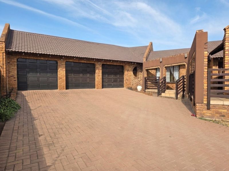 Front exterior view of the property featuring a triple garage, brick paved driveway, and facebrick facade with a tiled roof.