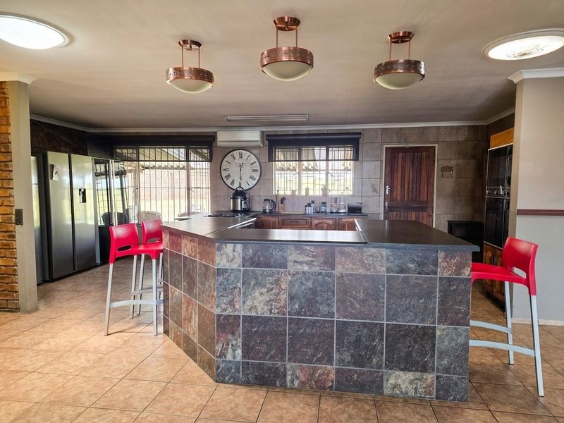 Spacious kitchen featuring a large stone-tiled island, built-in oven, tiled flooring, and distinctive copper pendant lighting, offering a functional and open layout.
