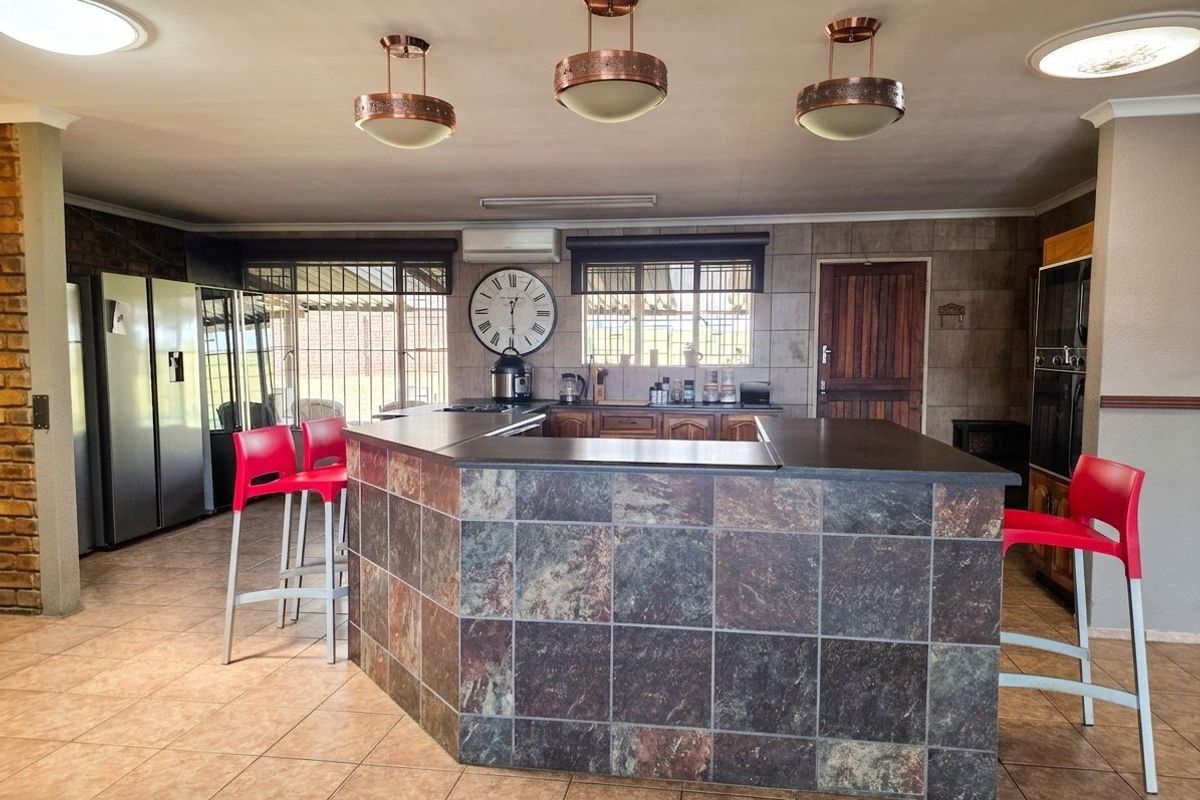 Spacious kitchen featuring a large stone-tiled island, built-in oven, tiled flooring, and distinctive copper pendant lighting, offering a functional and open layout.