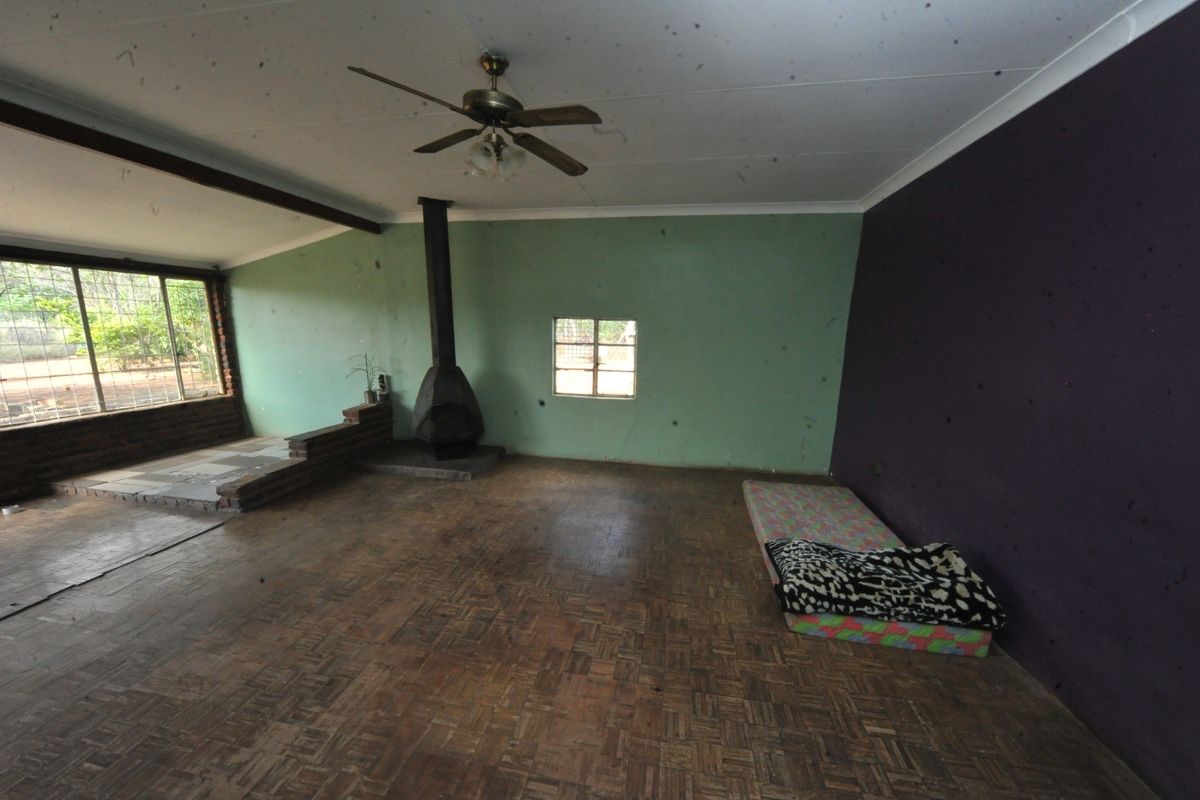 Spacious living area featuring parquet flooring, a freestanding fireplace, and a ceiling fan, offering a blank canvas for renovation.