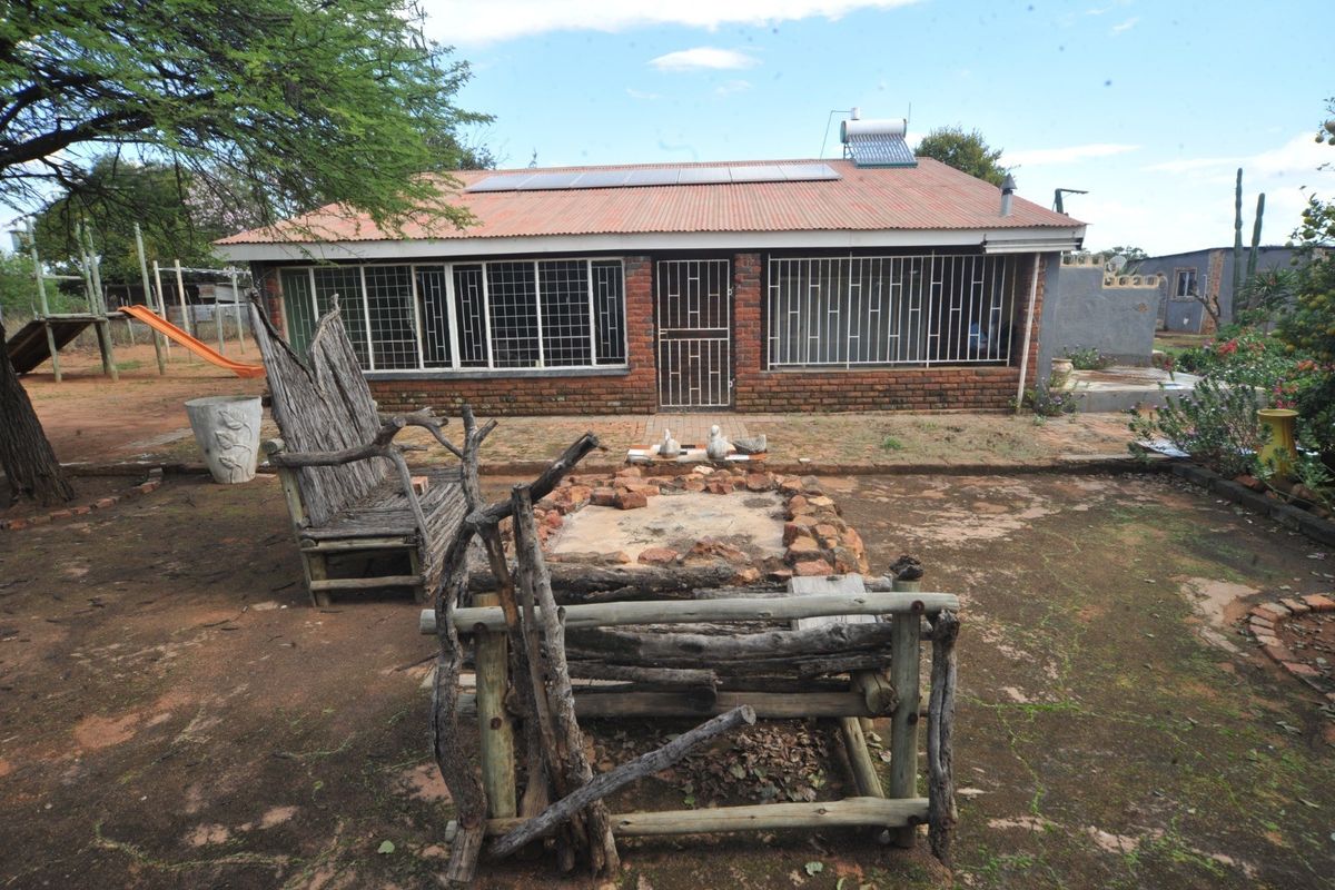 Rear view of a brick farmhouse featuring a corrugated metal roof, solar water heating system, solar panels, and a paved outdoor fire pit area.