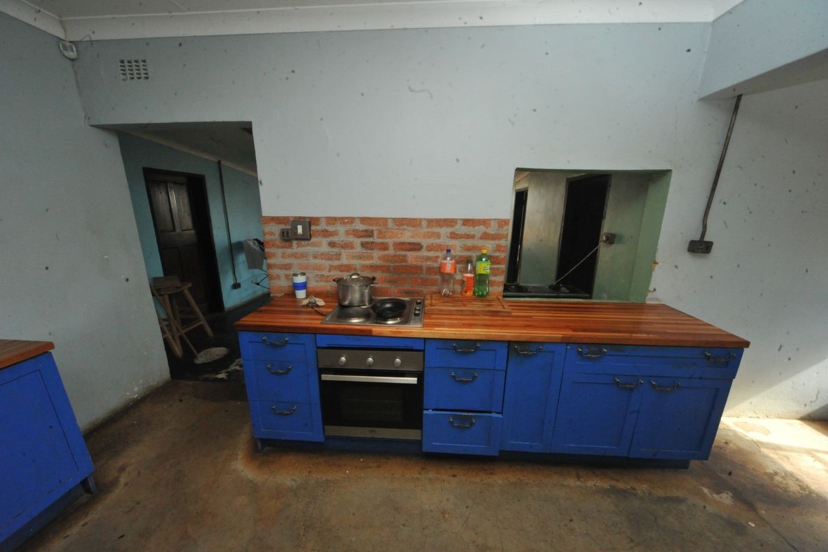 A rustic kitchen area featuring blue cabinetry, a wooden countertop, an integrated oven and hob, and an exposed brick backsplash.