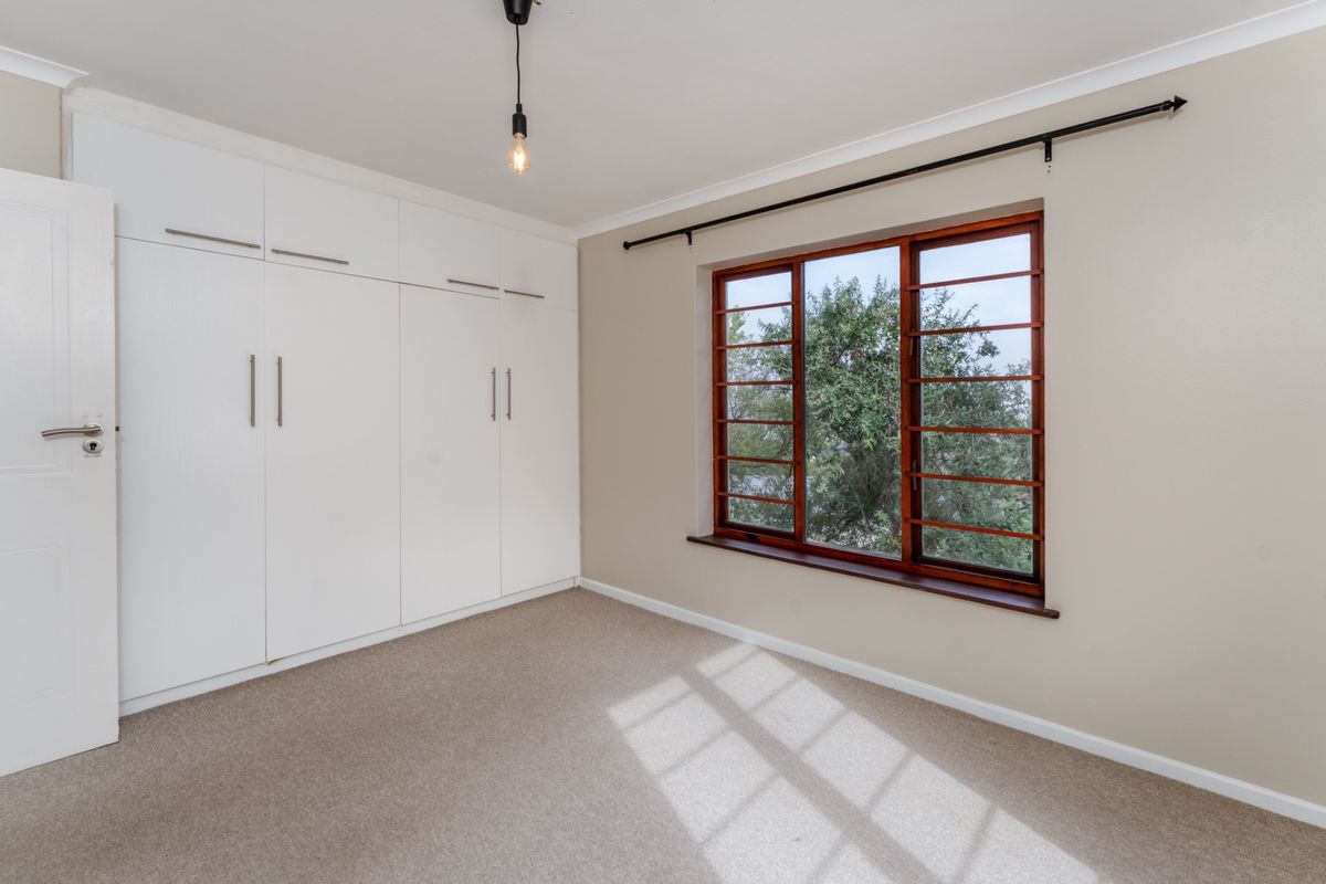 A bright, empty bedroom featuring neutral walls, carpeted flooring, and extensive built-in white cabinetry with modern hardware.