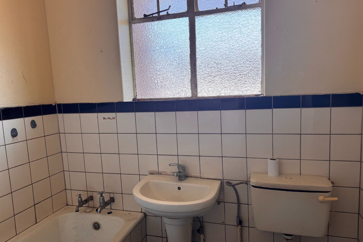 A dated bathroom featuring a pedestal basin, bathtub, and toilet cistern with original wall tiling and an obscured glass window.