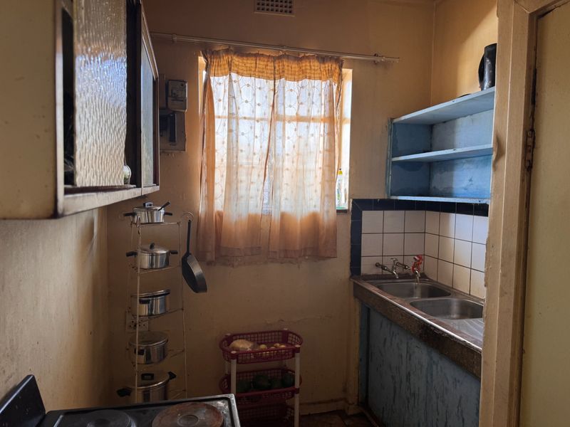 A compact, dated kitchen featuring a double bowl sink, tiled splashback, and original cabinetry, offering significant potential for a modern renovation.