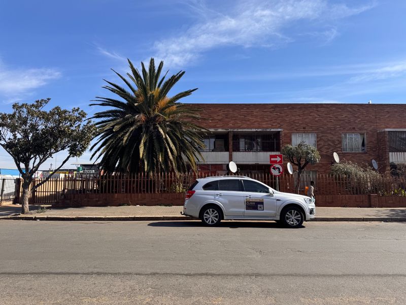 Street-level view of a brick apartment building facade featuring metal security fencing and satellite dish installations.