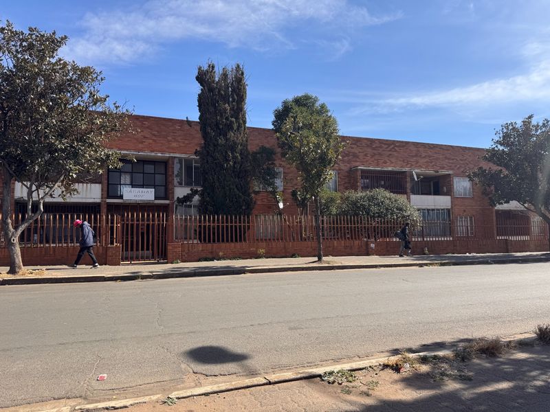Street view of a multi-story brick apartment building featuring secure metal fencing and balconies.