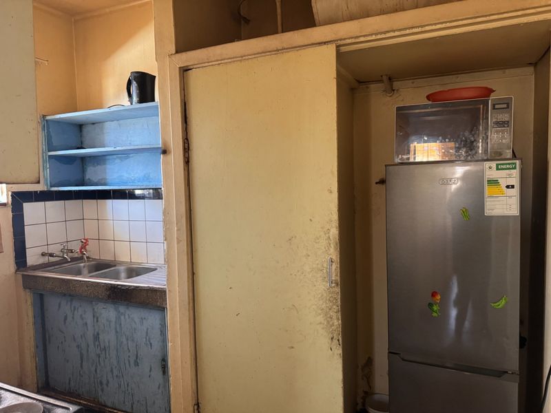 A dated kitchen featuring a double bowl stainless steel sink, tiled splashback, and built-in cabinetry requiring renovation and cosmetic updates.