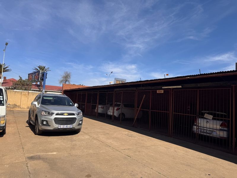 A row of secure, gated parking bays with corrugated metal roofing and concrete flooring, providing covered vehicle storage.