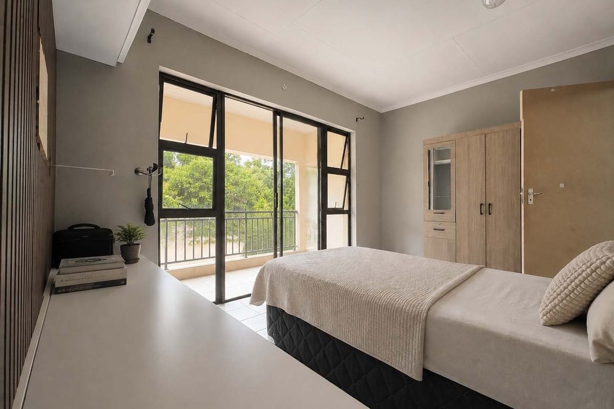 A well-lit bedroom featuring built-in cabinetry, modern slatted wall detailing, and direct access to a private balcony through large sliding glass doors.