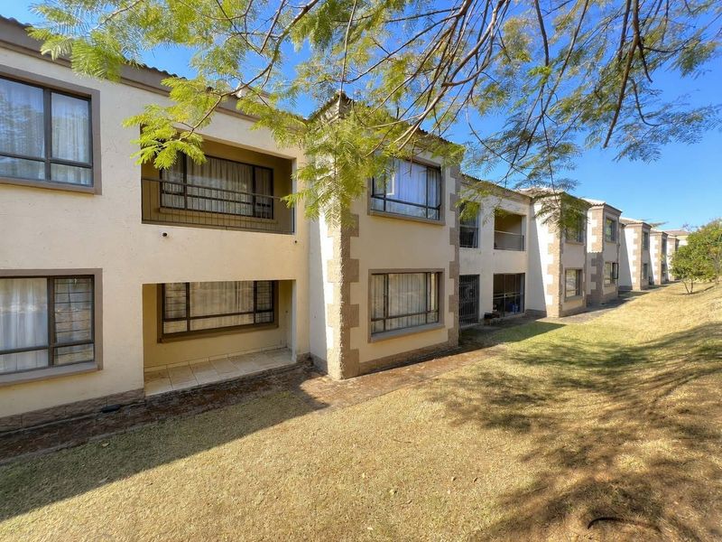 Rear elevation of a multi-story apartment complex featuring balconies, ground-floor patios, and paved walkways set against a landscaped garden area.