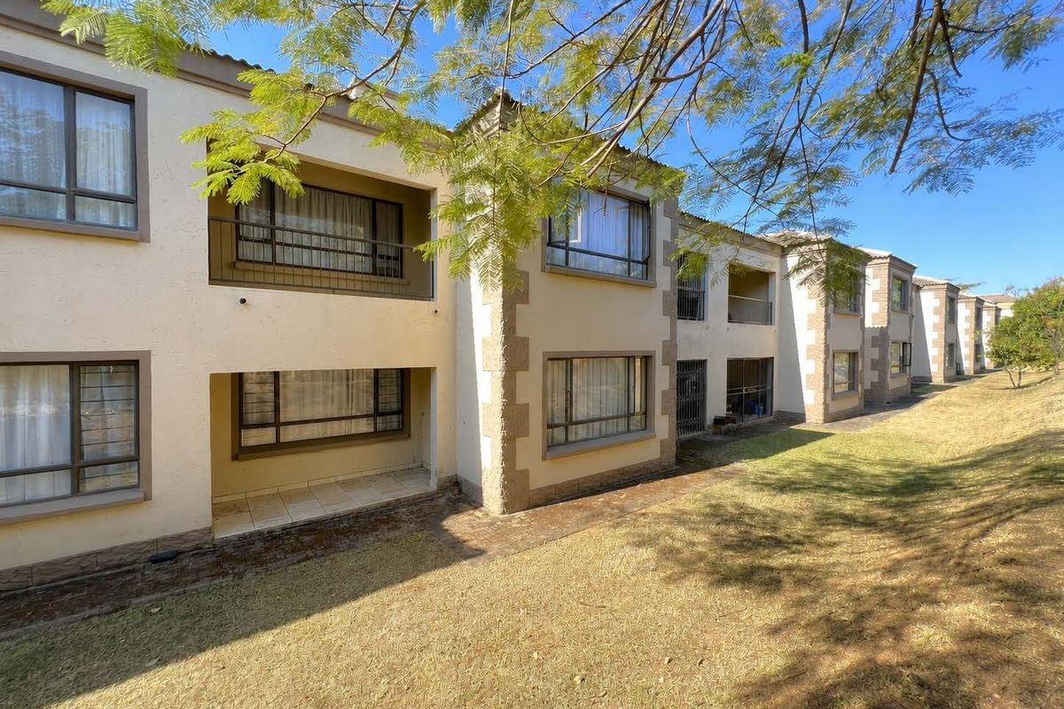Rear elevation of a multi-story apartment complex featuring balconies, ground-floor patios, and paved walkways set against a landscaped garden area.