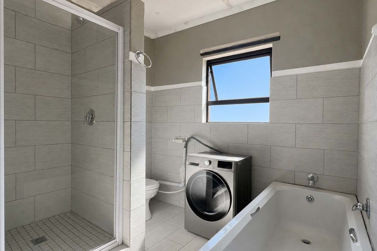 A functional bathroom featuring a shower enclosure, bathtub, and toilet, with neutral wall tiling and an unfinished ceiling requiring completion.