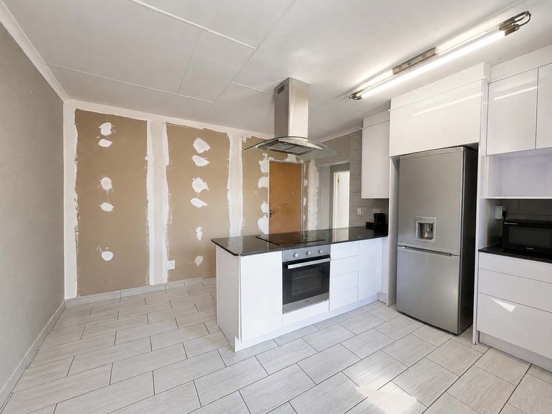 Kitchen area featuring modern white cabinetry, stone countertops, and built-in appliances, currently requiring wall finishing and painting to complete the space.