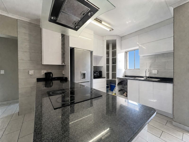 Modern kitchen featuring white high-gloss cabinetry, granite countertops, a glass extractor fan, and an integrated electric hob with tiled flooring.