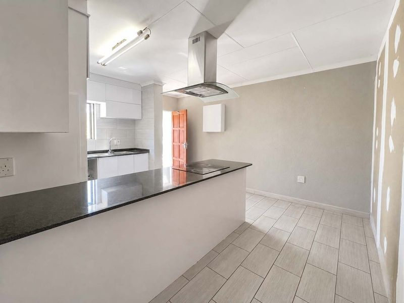 Open-plan kitchen area featuring a breakfast island, granite countertops, built-in hob, and extractor fan, with some wall areas requiring final finishing.