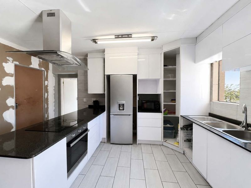 Modern kitchen featuring granite countertops, built-in oven, hob, and extractor fan, with white cabinetry and tiled flooring. Requires finishing of wall surfaces.