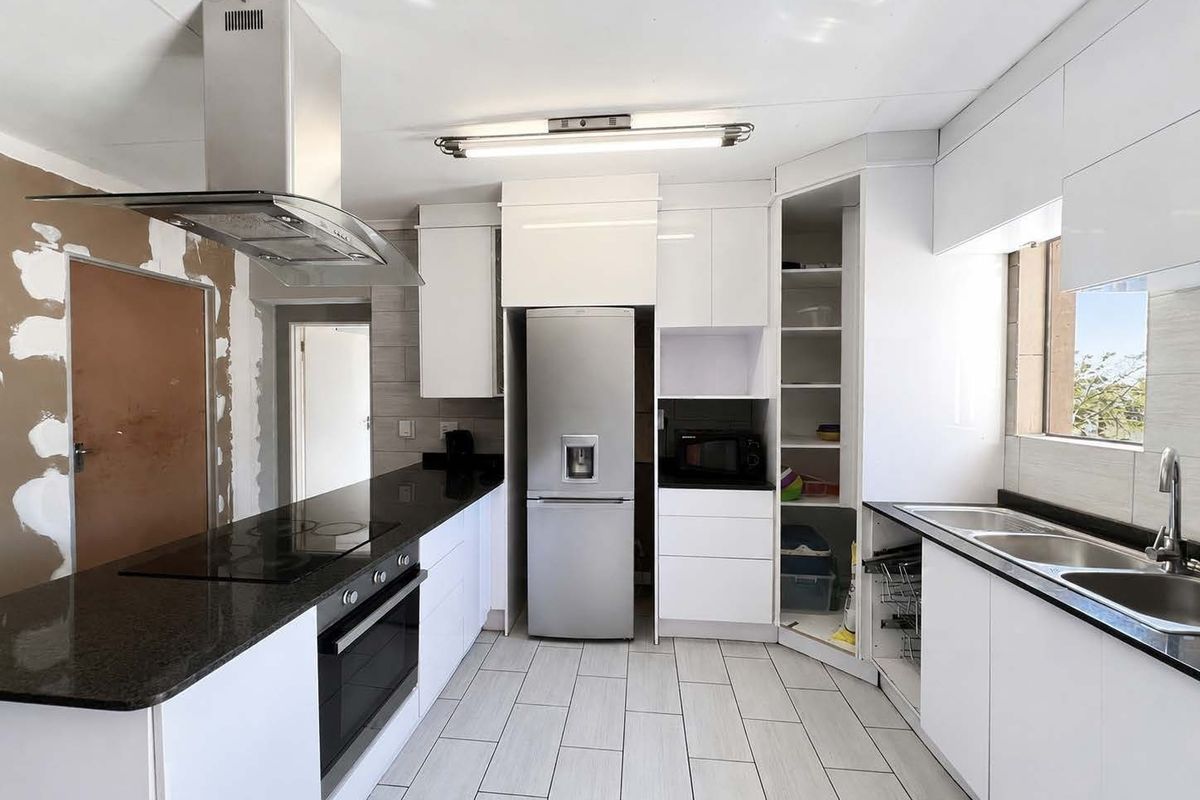 Modern kitchen featuring granite countertops, built-in oven, hob, and extractor fan, with white cabinetry and tiled flooring. Requires finishing of wall surfaces.