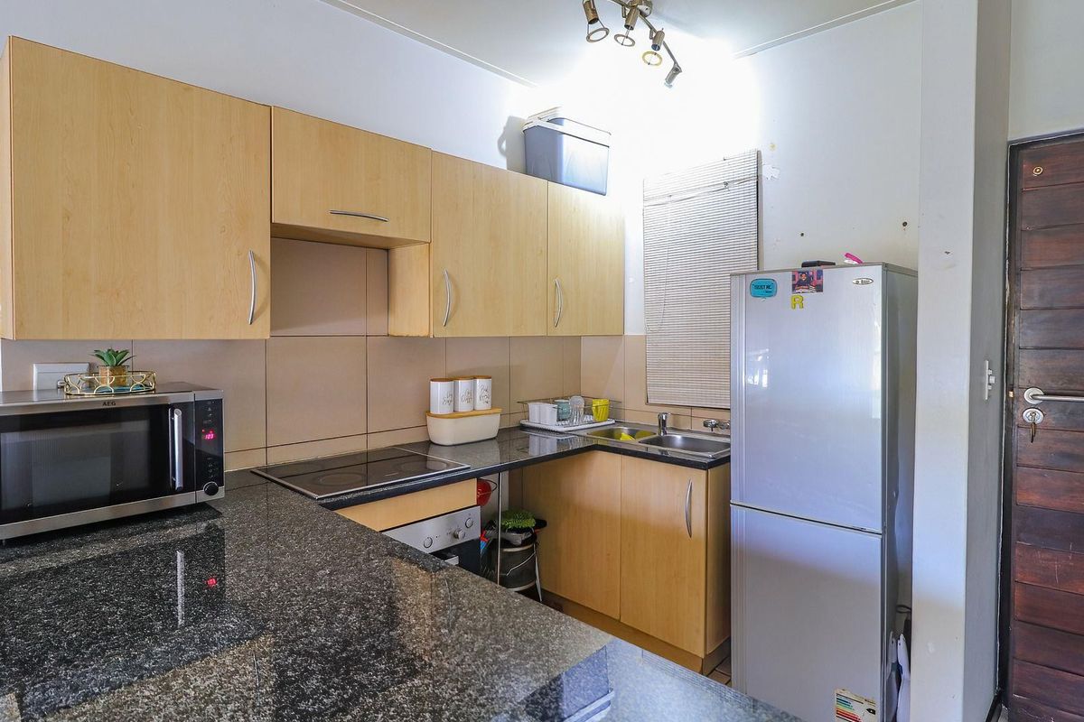 Compact kitchen featuring granite countertops, light wood cabinetry, built-in electric hob and oven, and a stainless steel sink with tiled splashback.