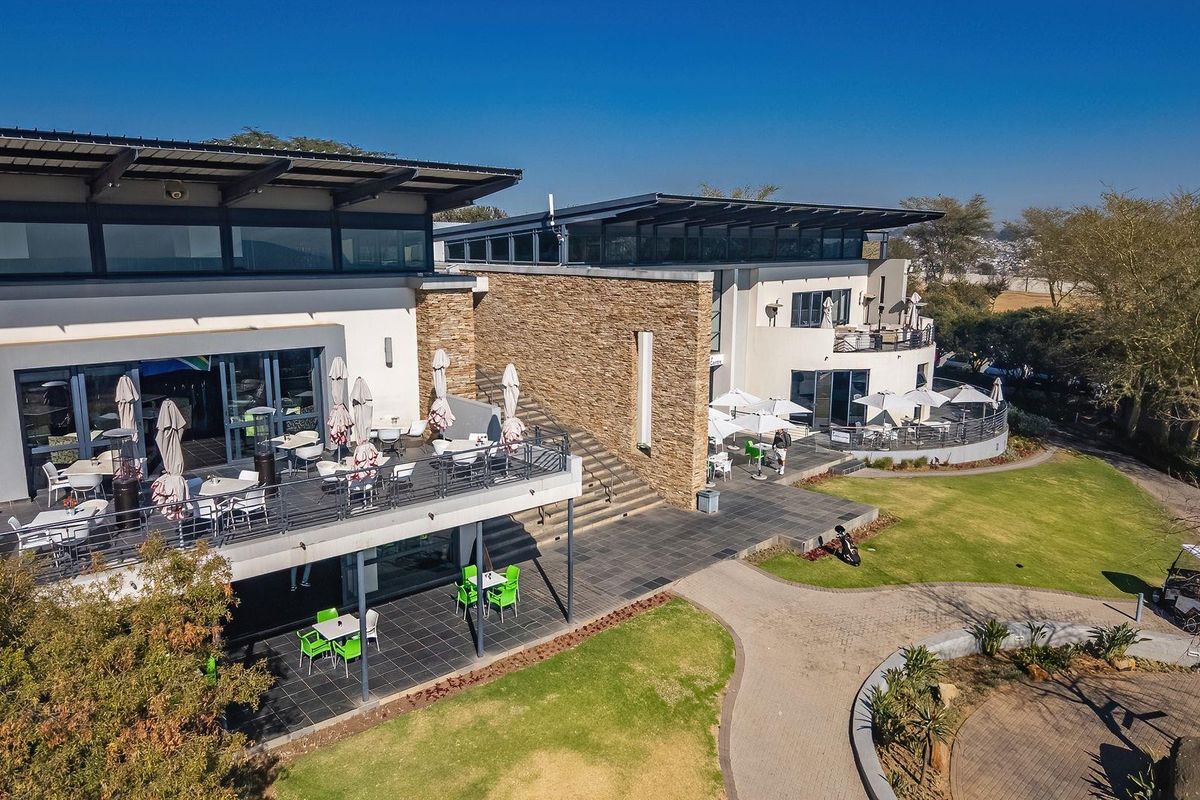 Aerial view of a modern multi-level building featuring stone cladding, expansive tiled patios, and well-maintained landscaped gardens.