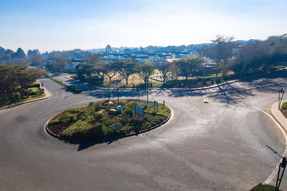 An aerial view of a paved roundabout and surrounding landscaped estate grounds, showcasing the property's neighborhood approach and infrastructure.