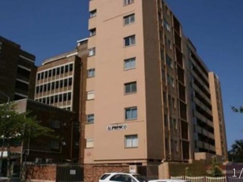 Exterior view of the multi-story Al Fresco apartment building featuring a tan facade and gated street-level entrance.