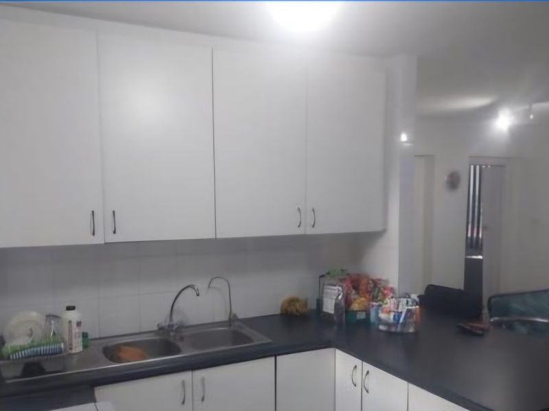 A functional kitchen featuring white cabinetry, dark laminate countertops, and a stainless steel double sink with a tiled splashback.
