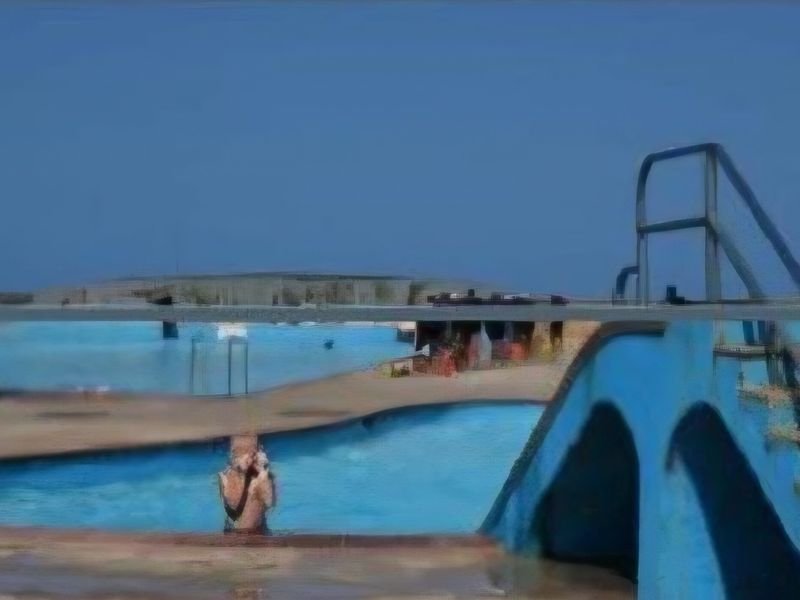 Outdoor swimming pool area featuring a blue slide and ladder, showing signs of wear and weathering.