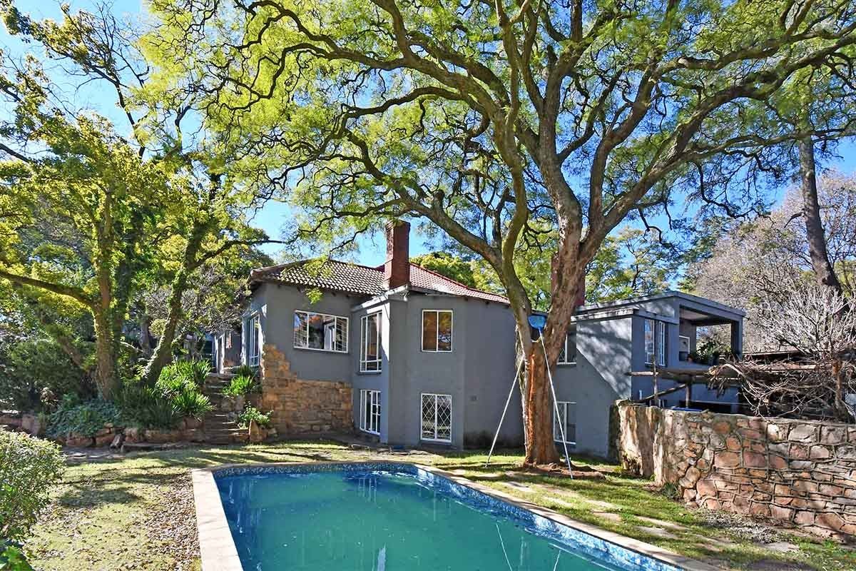 Rear view of the house featuring a swimming pool, stone retaining walls, and mature trees set against the building's exterior facade.