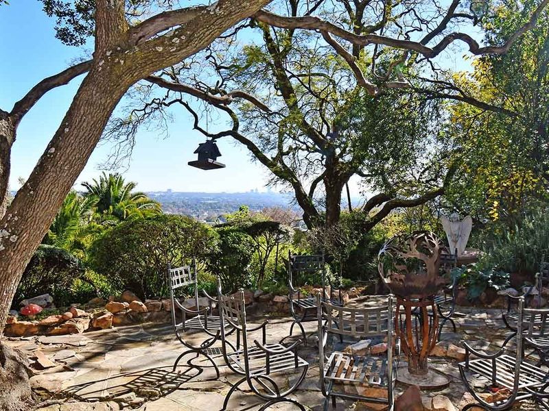 A scenic outdoor patio area featuring natural stone paving, mature trees, and an elevated view of the surrounding landscape.