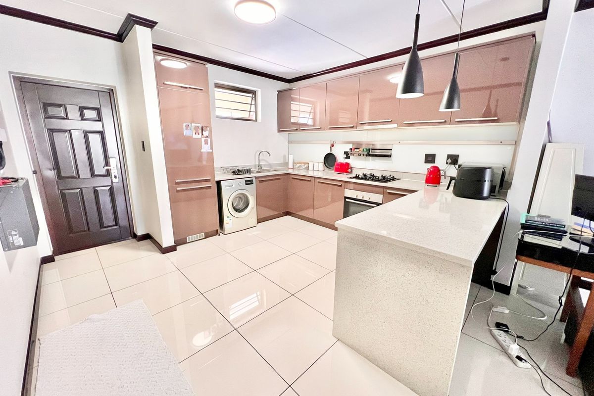 Modern kitchen featuring high-gloss cabinetry, stone countertops, a central island, and integrated appliances, complemented by sleek tiled flooring and contemporary pendant lighting.