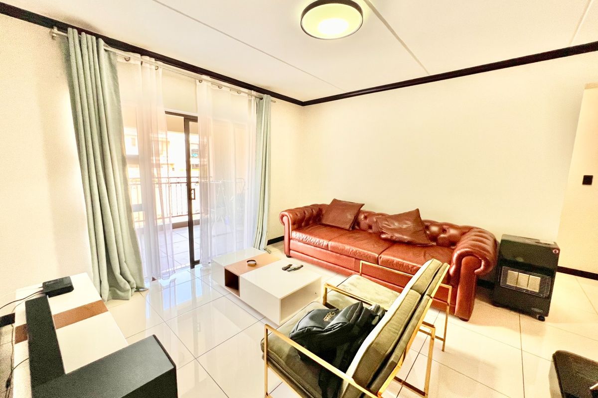 A bright living room featuring polished tiled flooring and direct access to a private balcony through a sliding glass door.