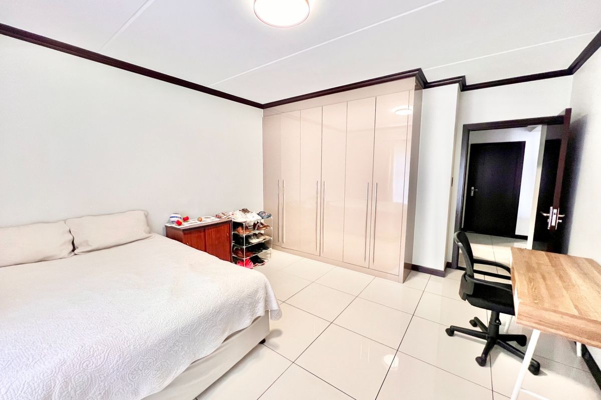 A spacious bedroom featuring neutral tiled flooring, dark crown molding, and extensive built-in cabinetry for ample storage.
