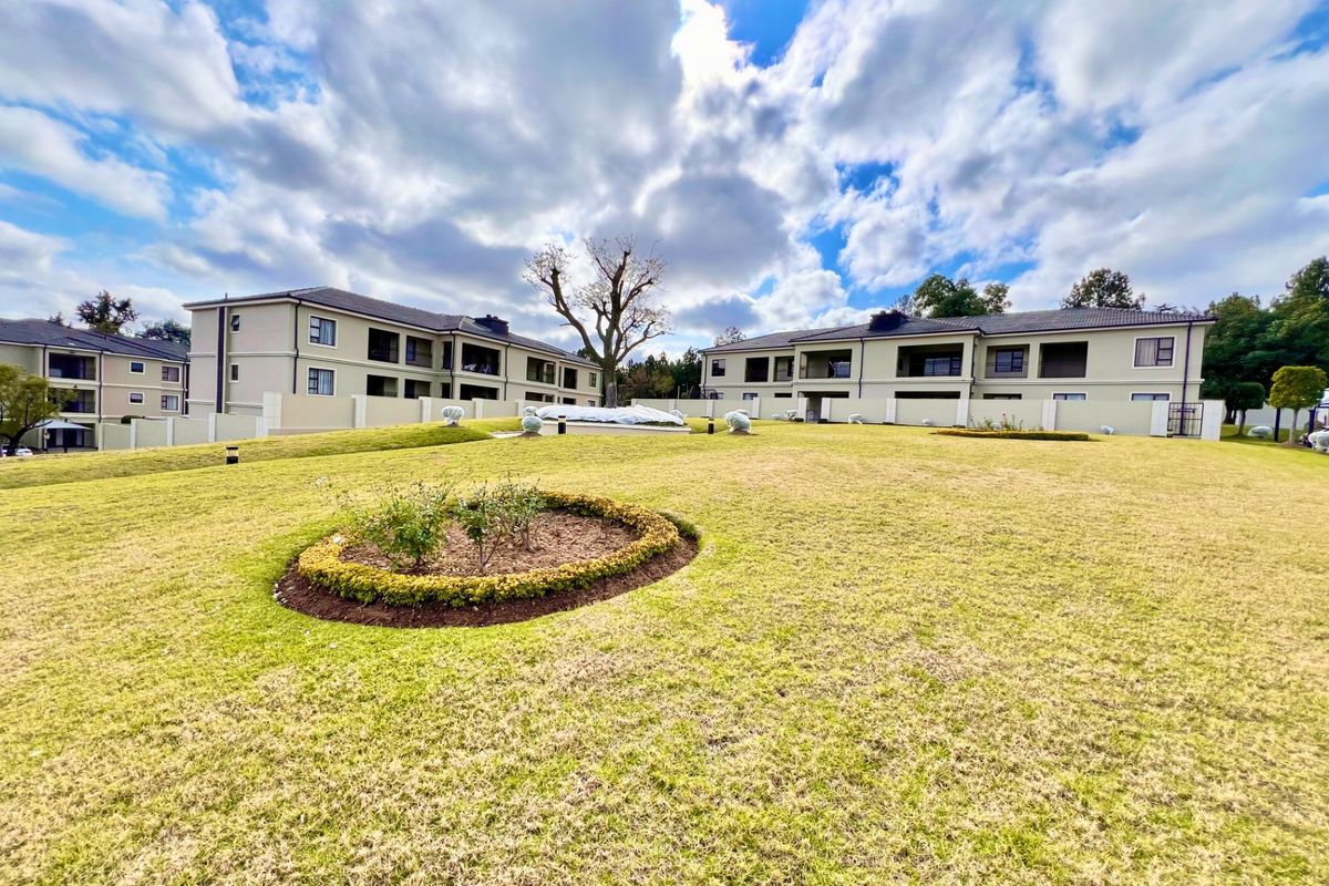 A well-maintained communal garden area featuring manicured lawns and landscaped beds, set against the rear facade of modern apartment buildings.