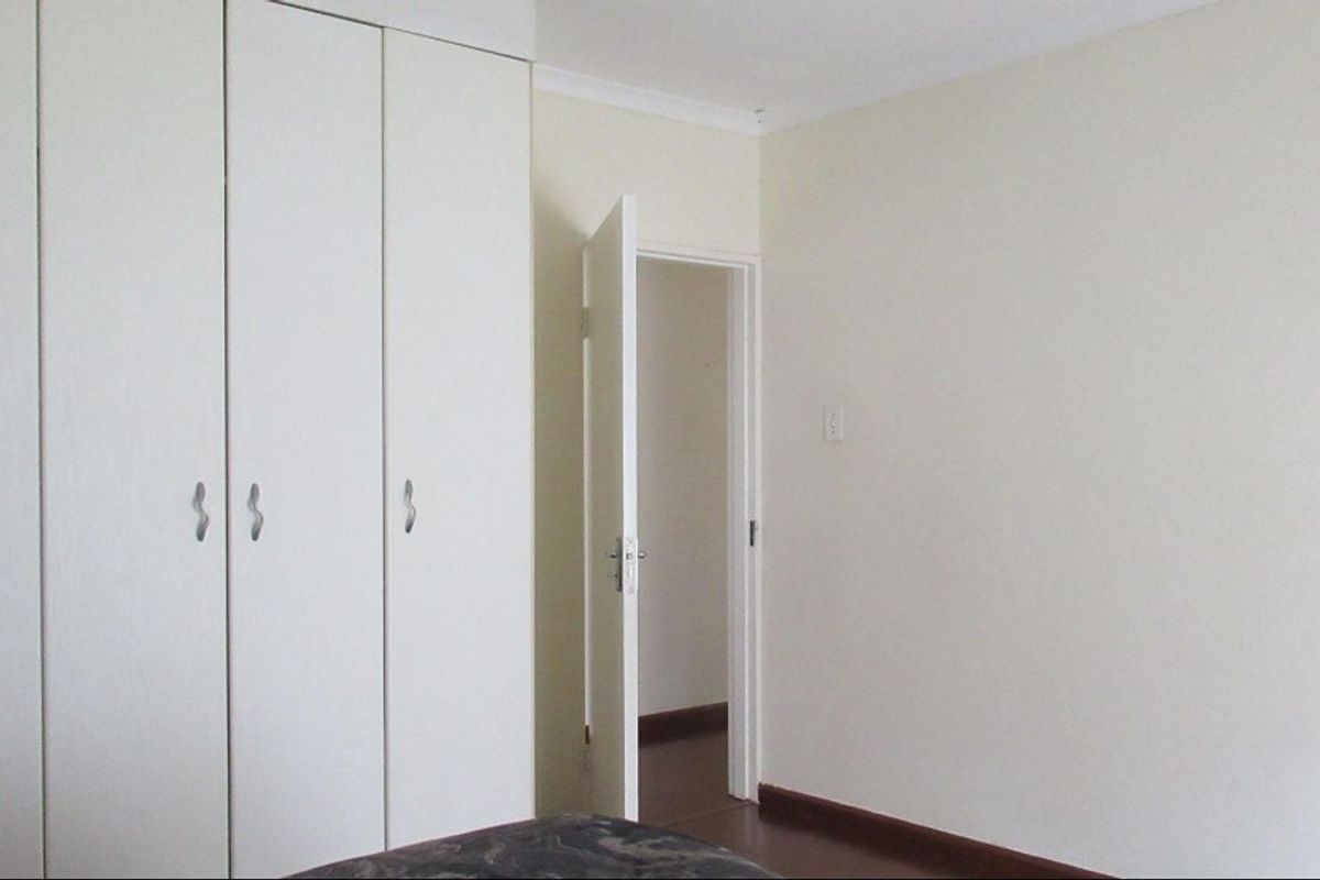 A clean, empty bedroom featuring neutral walls, built-in cupboards, and dark laminate flooring, offering a blank canvas for personalization.
